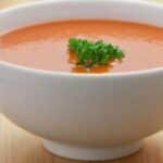 Tomato Soup Recipe showing the finshed bowl of soup ina white ceramic bowl on a wooden table