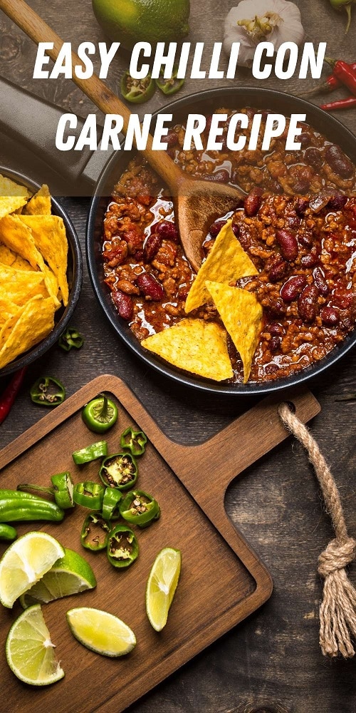 chili con carne in a pan with green chilies on a chopping board with some nachos in a bowl