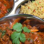 lamb curry in a silver balti dish with a bowl of rice