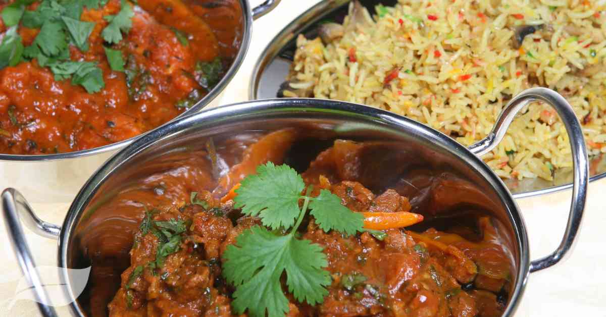 lamb curry in a silver balti dish with a bowl of rice