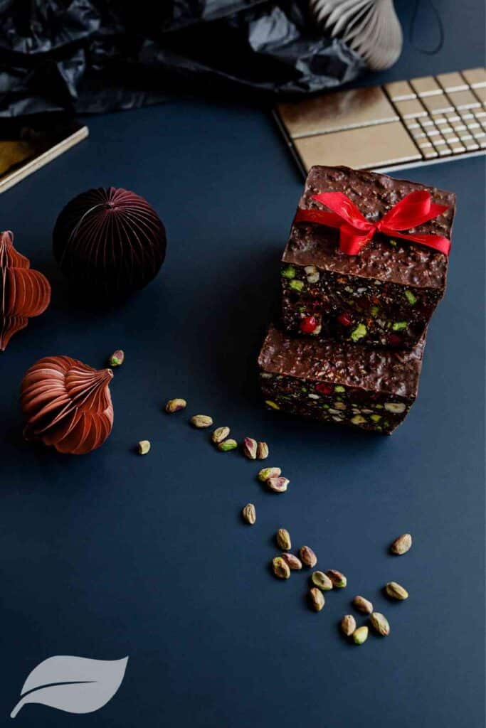 two squares of vegan chocolate cake on top of each other with a red bow and nuts