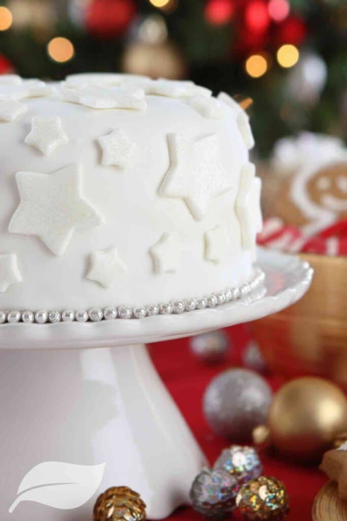 White Christmas cake on a white stand with Christmas baubles in the background