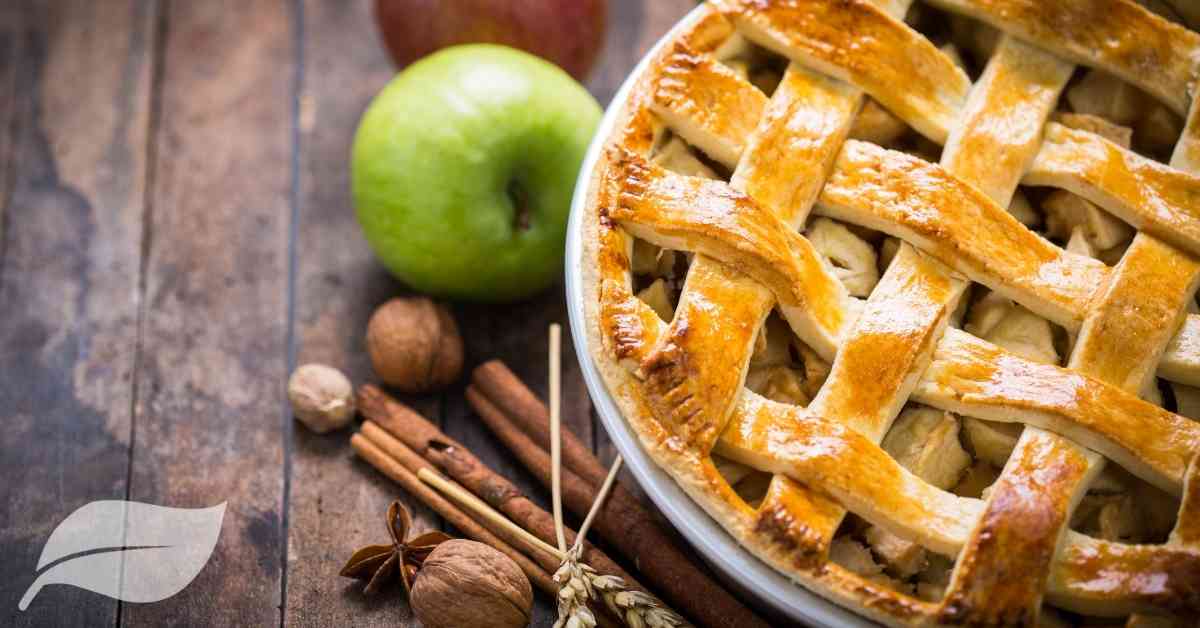 showing only half or an apple pie with cinnamon and a red and a green apple to the left