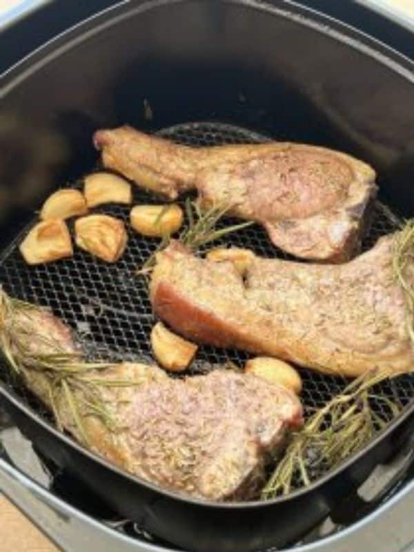 3 lamb chops in an air fryer basket with small roasted potatoes