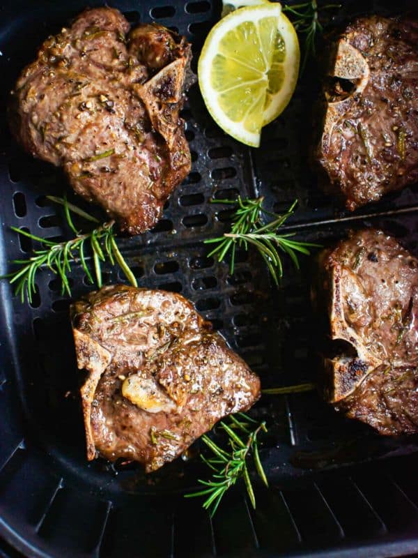 4 Air Fried Lamb Chops in an air fryer basket with sprigs of dill and half a lemon