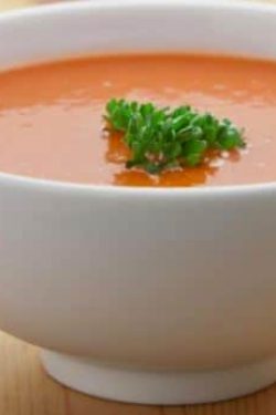 Tomato Soup Recipe showing the finshed bowl of soup ina white ceramic bowl on a wooden table